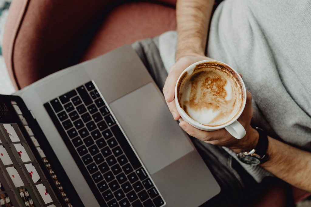 Person holding a cup of coffee while working on a laptop, symbolizing how people try to fight brain fog with caffeine